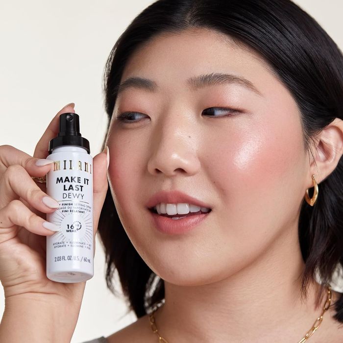 A model showcasing Milani's Make It Last Dewy setting spray, positioned near their face with a joyful demeanor
