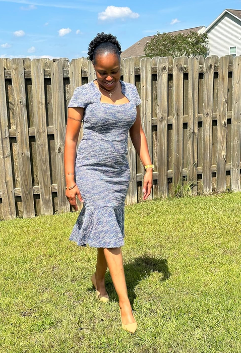 A reviewer wearing a fashionable knee-length dress featuring short sleeves and a flounce hem, strolling on a grassy area.