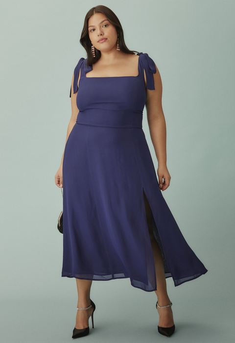 A model wearing a chic blue dress featuring ribbon-tied shoulders and a mid-length hem, styled with black heels.