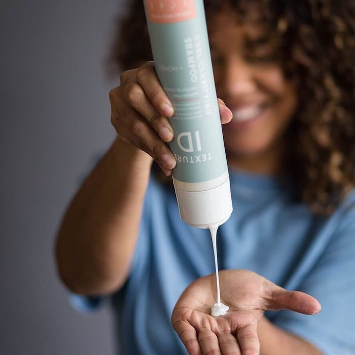 A model demonstrating the use of shampoo by squeezing it into their hand.