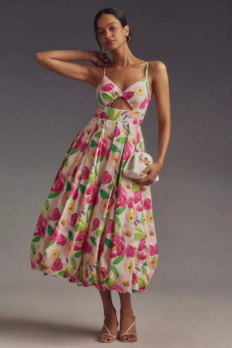 A woman dressed in a floral outfit, posing with one hand on her hip and holding a clutch.