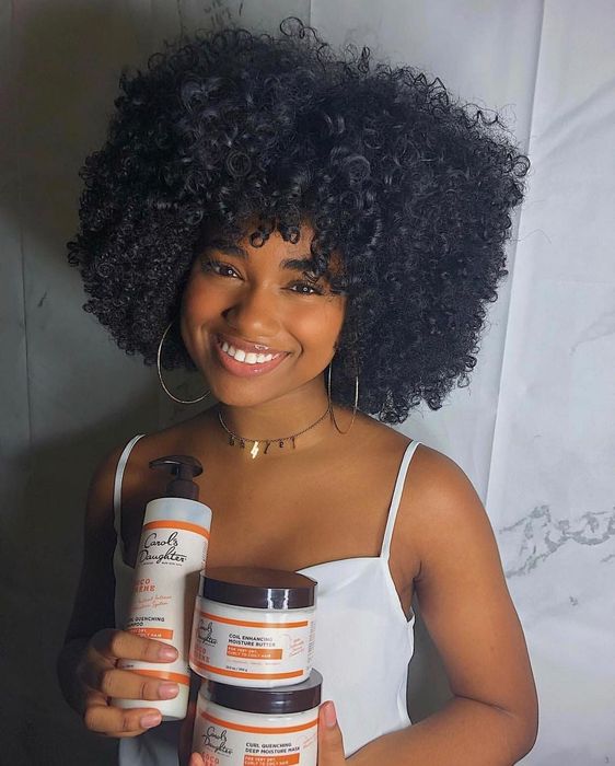 A person holding the shampoo along with other curl-enhancing products