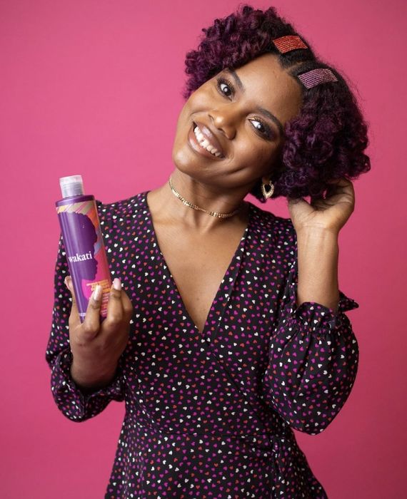 A person in a colorful heart-patterned dress is holding a bottle of detangling conditioner, ready to give their hair a flawless finish.