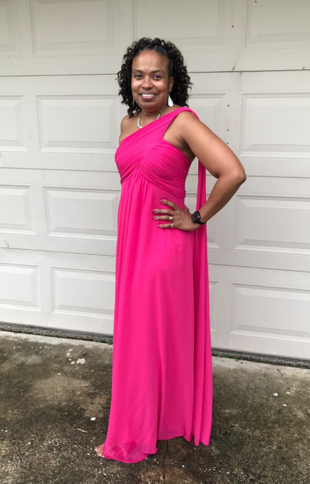 A reviewer is elegantly posing in a one-shoulder pink gown, hand on hip.