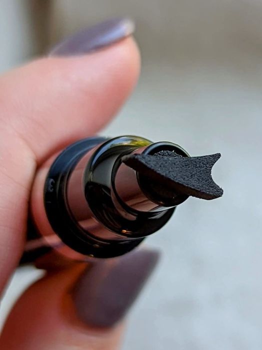 A reviewer holding the eyeliner pen, which has a wing-shaped stamp for easy application