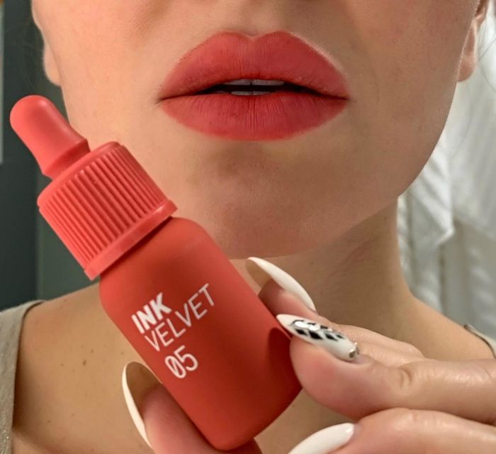 a reviewer showcasing the coral lip ink while holding the product
