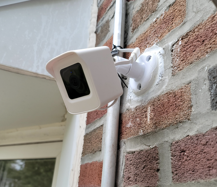 The security camera mounted on the exterior of a brick wall, keeping watch over the area.