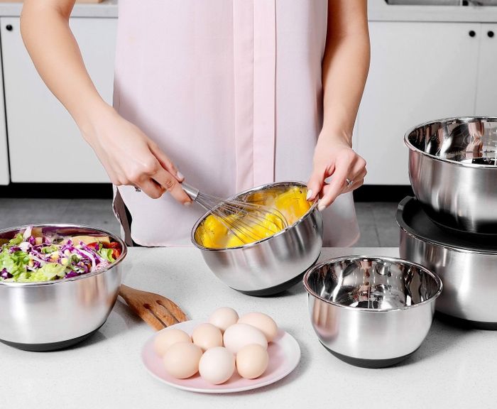 A model whisking eggs in one of the bowls, with additional ingredients neatly arranged in the others.