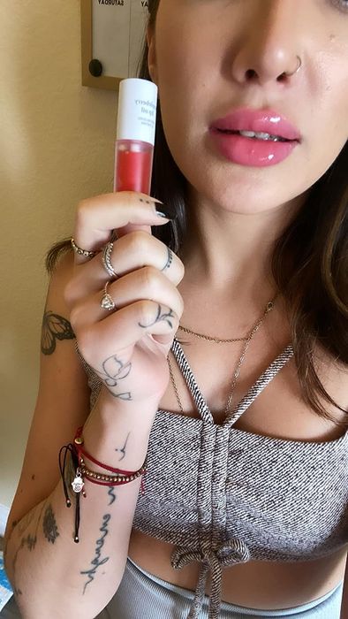 A reviewer holding the appleberry lip oil, with it applied to their lips