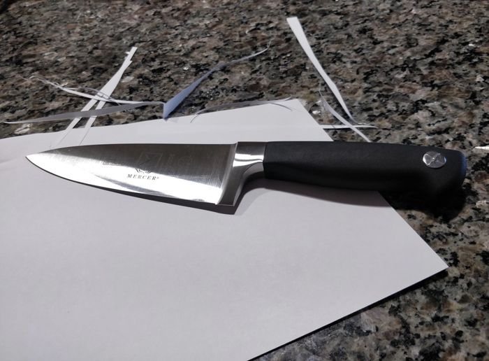 The chef's knife resting on a piece of paper that has been neatly cut by the blade.