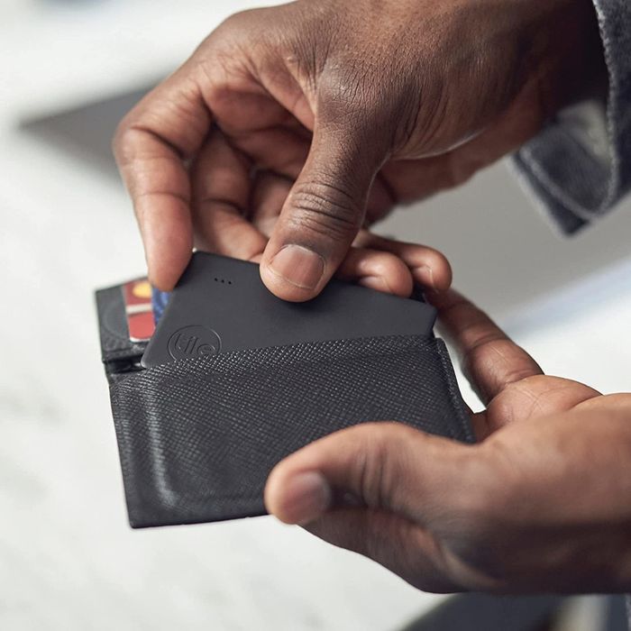 A hand pulls the black Tile Bluetooth tracker out of a wallet.