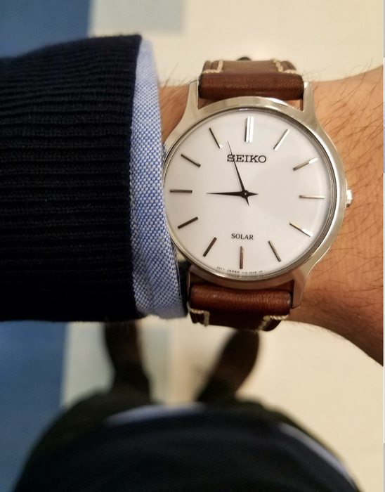 A reviewer’s wrist adorned with a white-faced Seiko watch, paired with a brown leather strap.