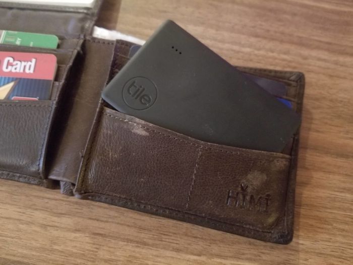 A black Bluetooth tracker nestled inside a standard brown leather wallet card holder.