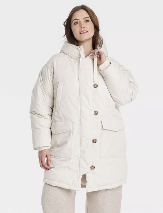 A person confidently posing in a long, padded coat with oversized buttons and large front pockets.