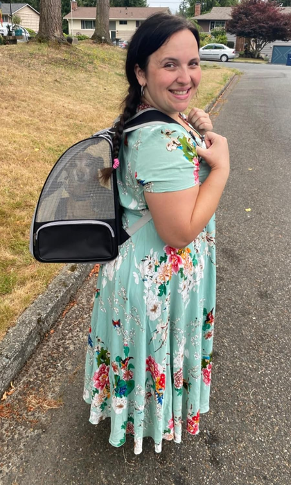 A reviewer in a floral dress smiles warmly while carrying a pet carrier, with a dog clearly visible inside.