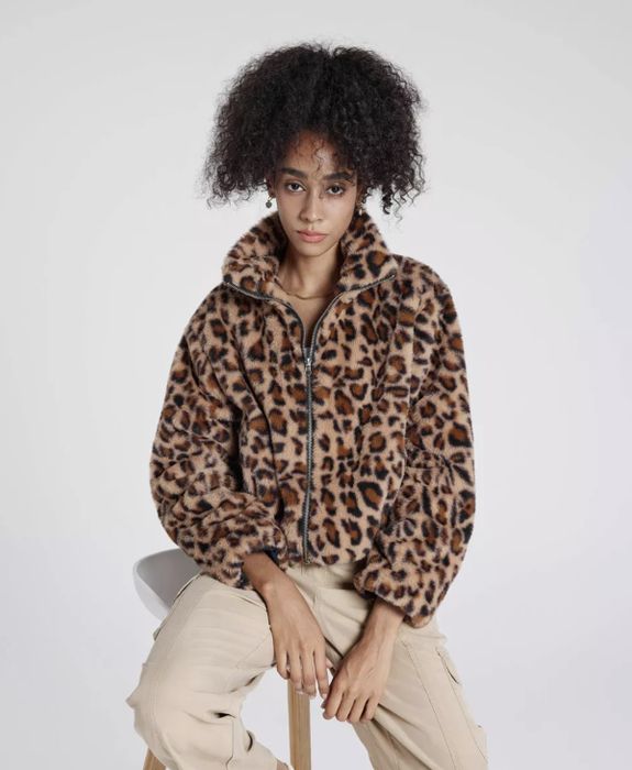 A person seated in a leopard print faux-fur jacket and beige pants, with natural hair styling