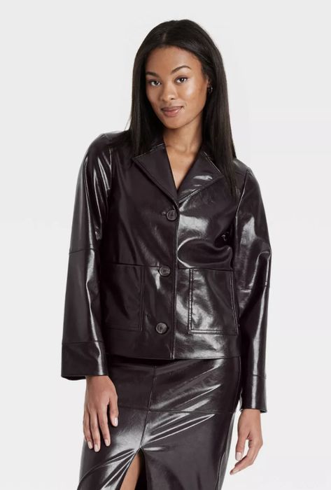 A person wearing a glossy, modern leather jacket paired with a skirt featuring a side slit, confidently striking a pose.