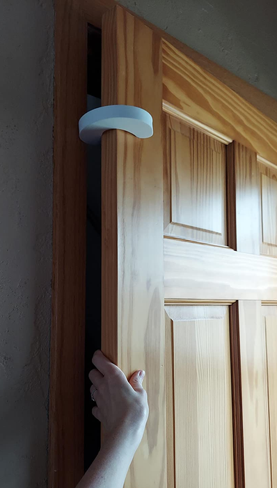 A reviewer showing a pinch guard installed at the top of the door with their hand in the gap it creates.
