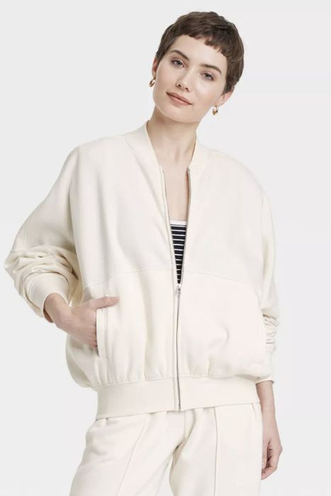 A person wearing an oversized casual jacket with hands tucked into the pockets, standing against a neutral background