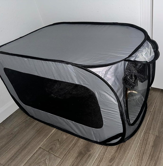 A portable fabric playpen for pets, featuring mesh sides and a zippered door, placed on a wooden floor.