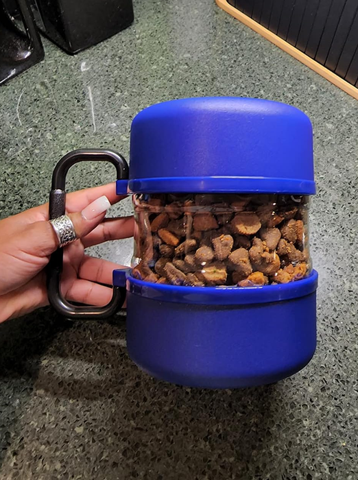 A person holding a sleek, portable blue pet treat container equipped with a clip, ideal for pet owners who are always on the move.