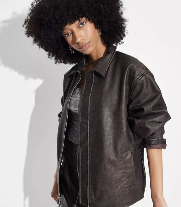 A person confidently posing in a stylish leather jacket over a patterned top, with a bold expression