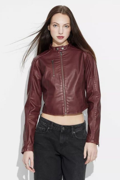 A person wearing a sharp leather jacket and dark jeans, standing confidently in front of a plain background