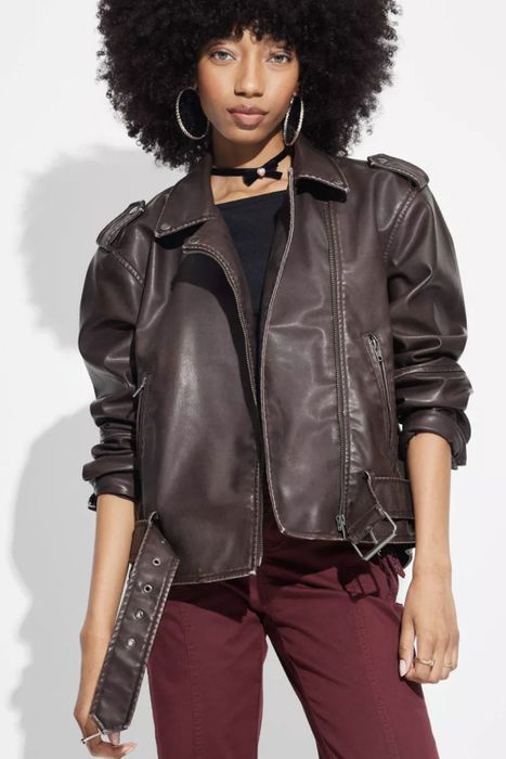 A person sporting a leather jacket, black top, and dark pants, posing with a confident demeanor