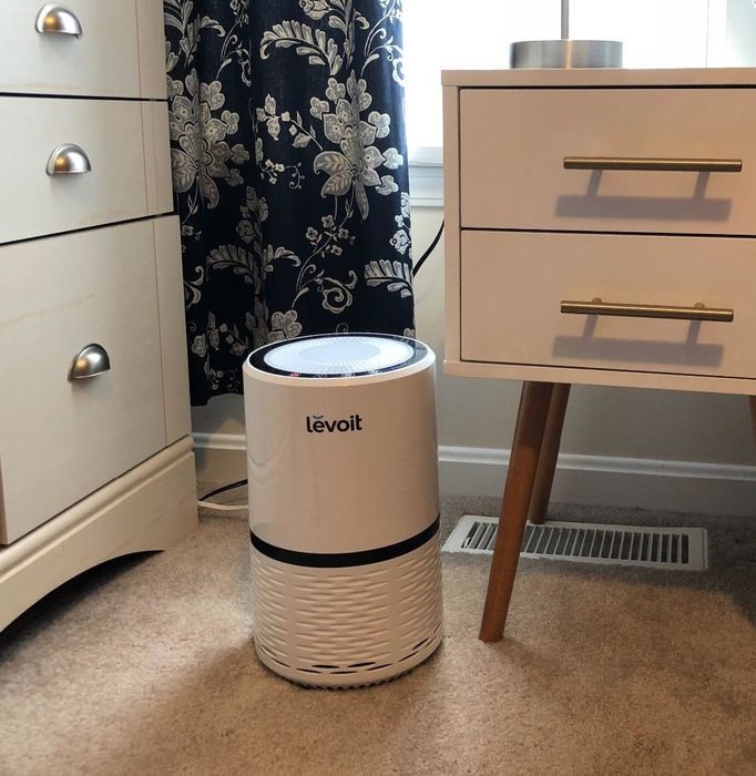 a white air purifier placed beside a nightstand