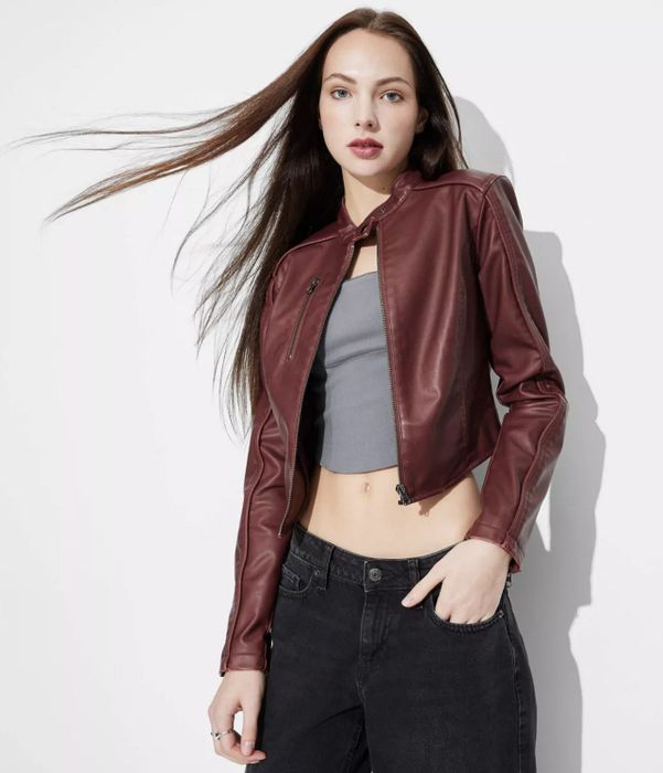 A person in a leather jacket, crop top, and jeans, confidently posing with hair flowing and a neutral expression