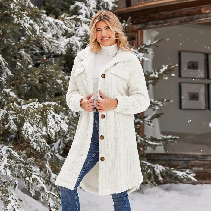 A person wearing a long ivory faux-fur coat, white turtleneck, and jeans, standing in a snowy outdoor scene with trees in the background