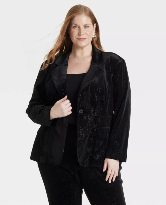 A person poses confidently in a sleek velvet suit, showcasing a stylish jacket with a single button.
