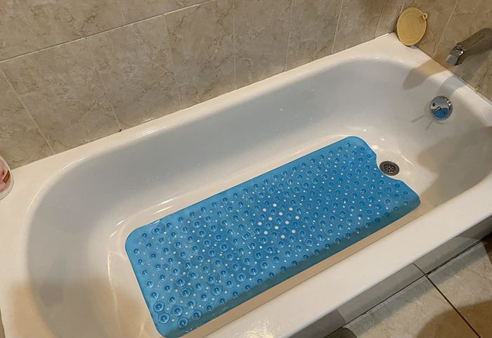 A reviewer’s photo of a blue pebble-textured bath mat placed in their bathtub