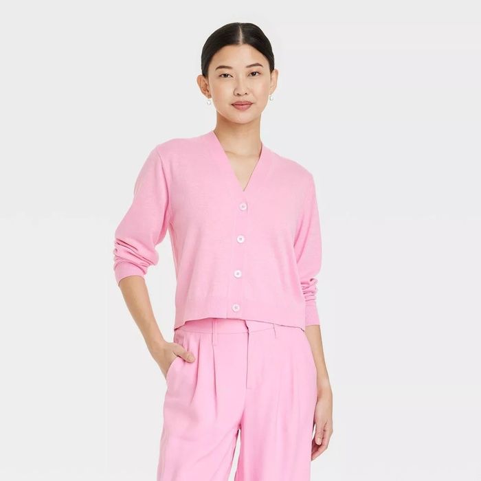 A person models a chic outfit featuring a button-up cardigan paired with pleated trousers