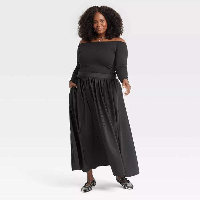 A person models an off-the-shoulder black top paired with a long, flowing skirt during a fashion shoot