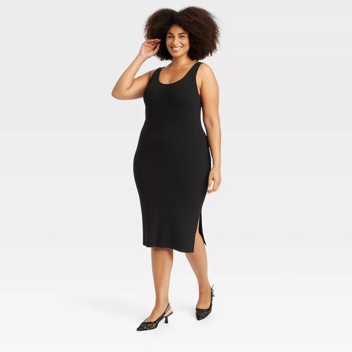 A model is showcasing a sleeveless, ribbed black midi dress featuring a side slit, styled with elegant pointy-toed heels.