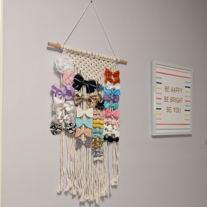 Reviewer's photo of a macrame hair accessory holder filled with vibrant bows, mounted on their child's bedroom wall