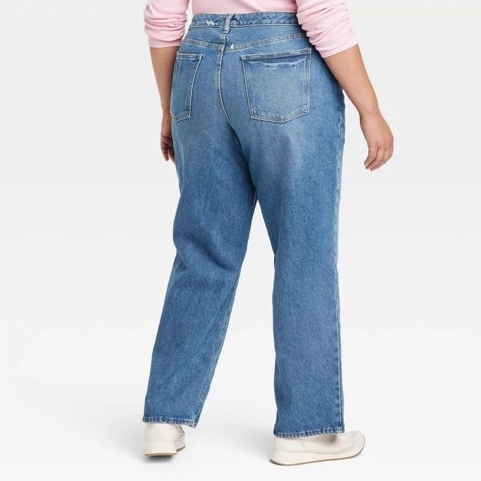 A person is photographed from behind, wearing high-waisted blue jeans paired with white sneakers.