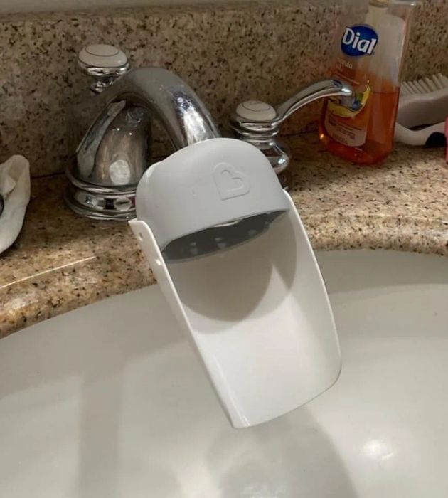 A bathroom sink equipped with a faucet extender and soap dispenser, accompanied by vibrant bath toys scattered on the counter