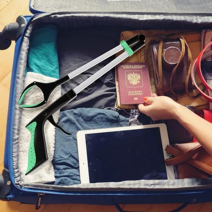 An open suitcase with a passport and tablet inside, with a hand reaching in beside a grabber tool.