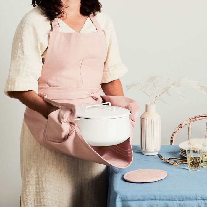 A model wearing a pink apron, holding a Dutch oven using the attached pot holders