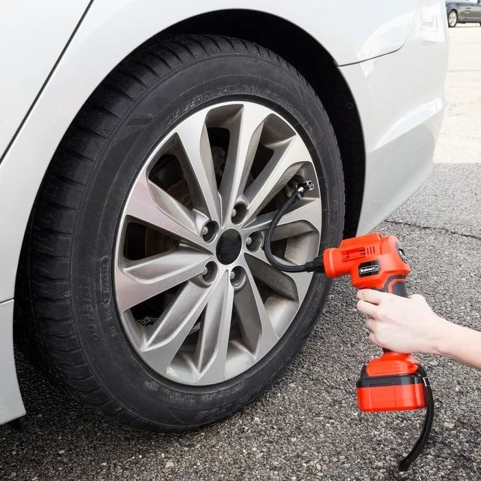 A person using a portable air compressor to inflate a car tire in a parking lot.