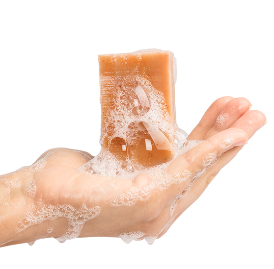 A model’s hand holding a bar of soap covered in suds