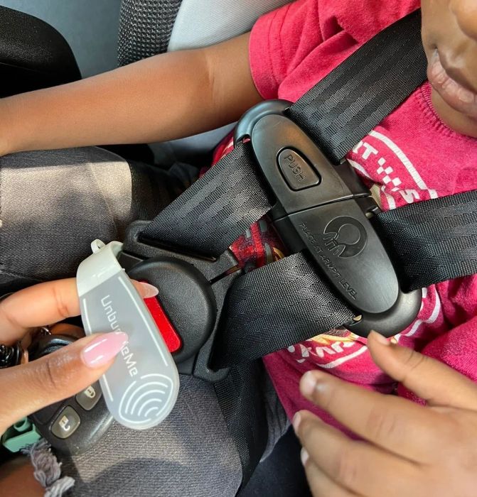 Close-up view of an adult using a specialized key tool to unbuckle a child's car seat harness