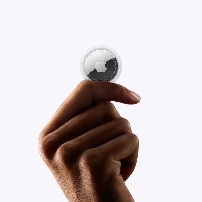 A hand holding an Apple AirTag, a small, round tracking device designed to help locate misplaced items.