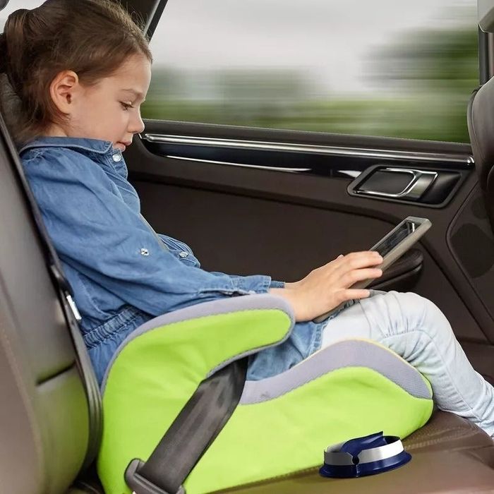 A child sitting in a car seat, using a tablet, with a sick bag visible and ready for quick use.