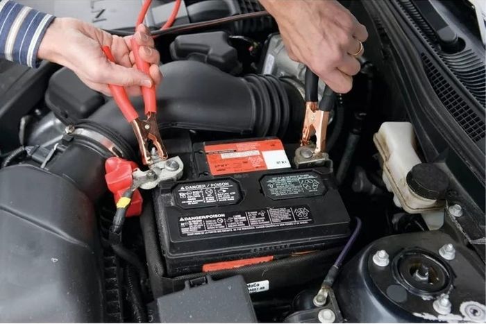 Hands connecting jumper cables to a car battery, working under the hood.