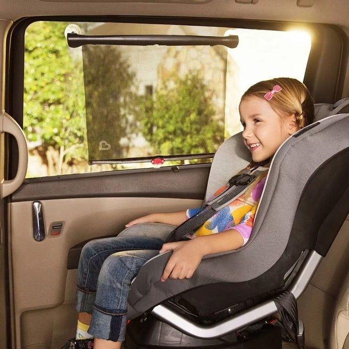 A child happily secured in a car seat, smiling, with a sunshade on the window of the vehicle.