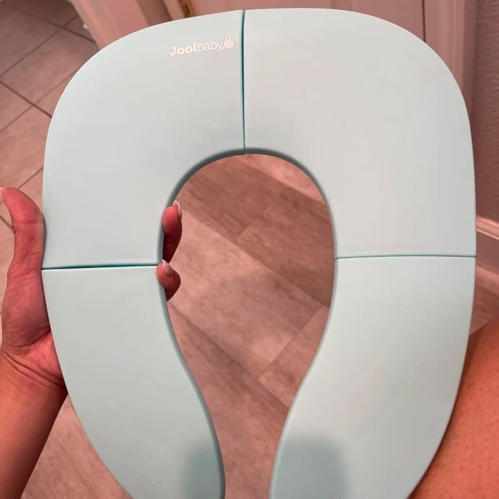 A person holds a Jool Baby folding travel potty seat, showcasing its sleek, portable design.