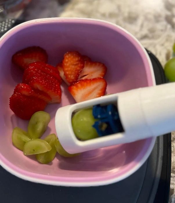 A reviewer’s photo of sliced strawberries and green grapes in a pink bowl, with a white handheld grape slicer in action.